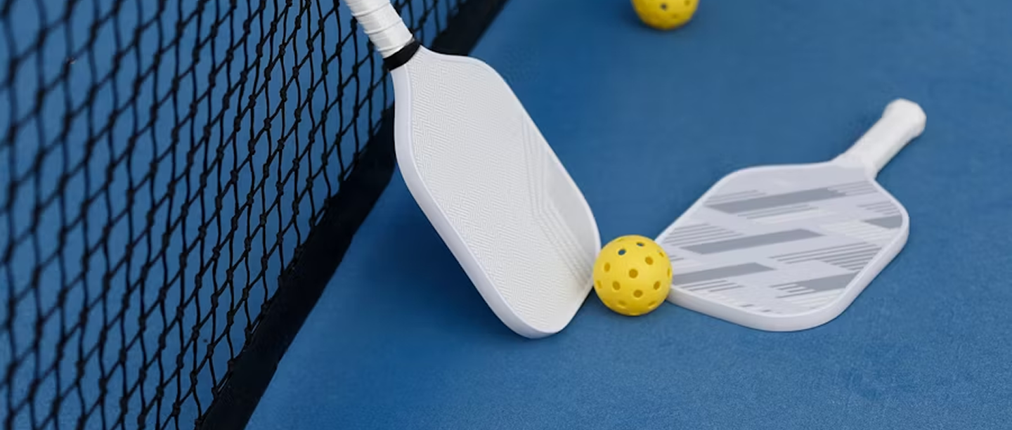 two white pickleball paddle in the court floor besides the net with a ball