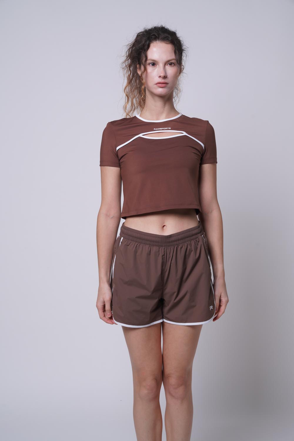 Female model posing with a straight body, wearing ramsport arcBand crew tee in brown