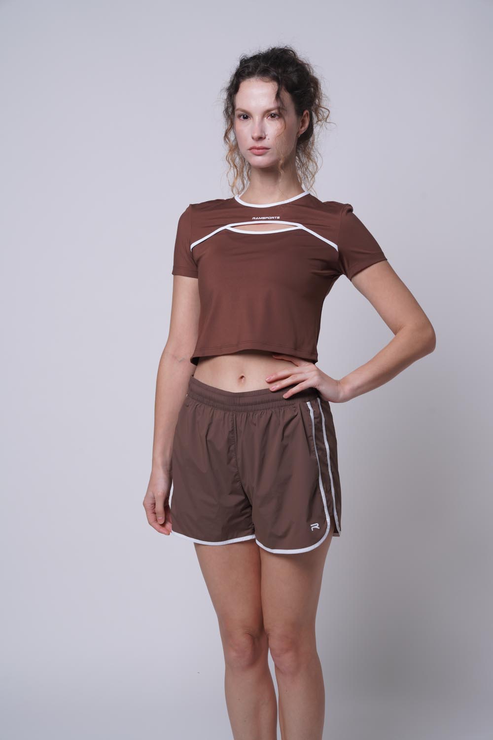 Female model with her hand on her left hip wearing Ramsport arcBand crew tee
in brown