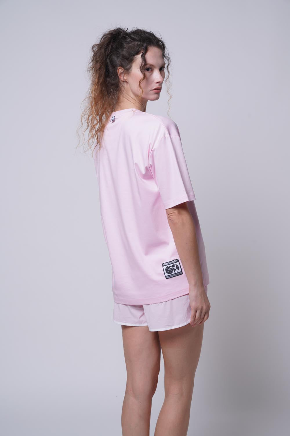 female model standing sideways wearing Ramsports Court Moods Icon Grid T-shirt in pink