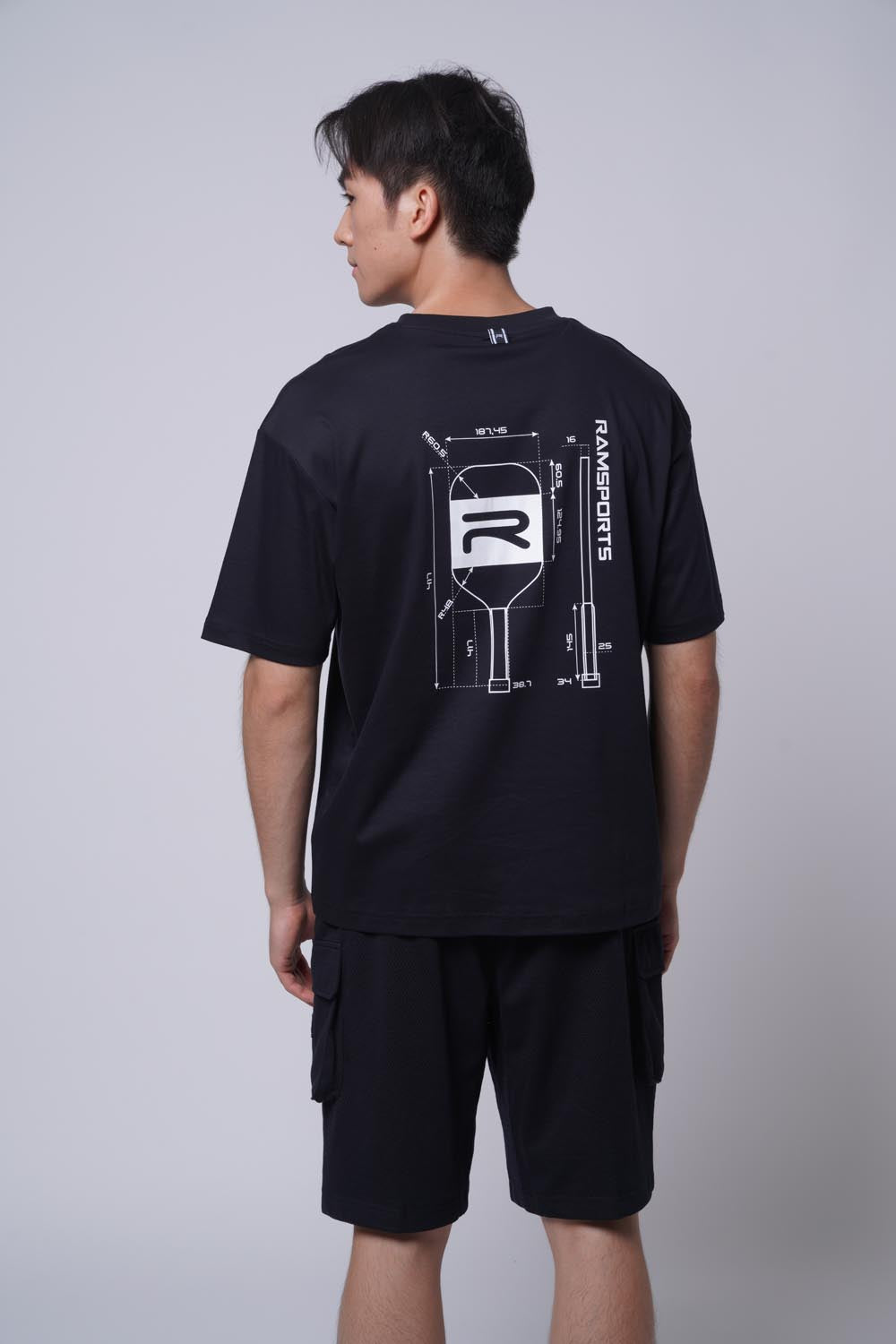 Back view of male model wearing a black Ramsports Blueprint Back Graphic tee with black shorts