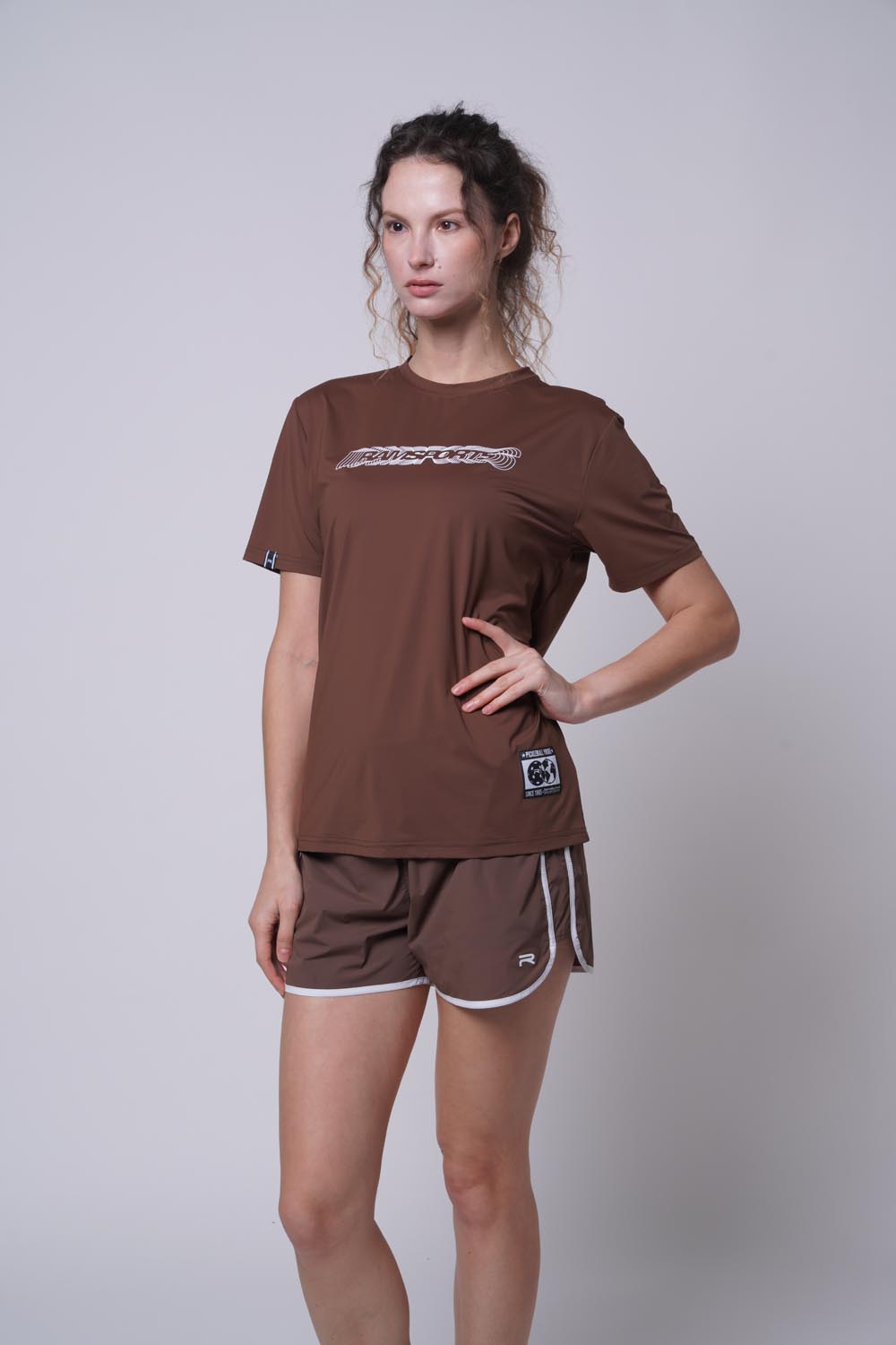 female model wearing the brown Ramsports Playbook Court Diagram Tee on a plain background