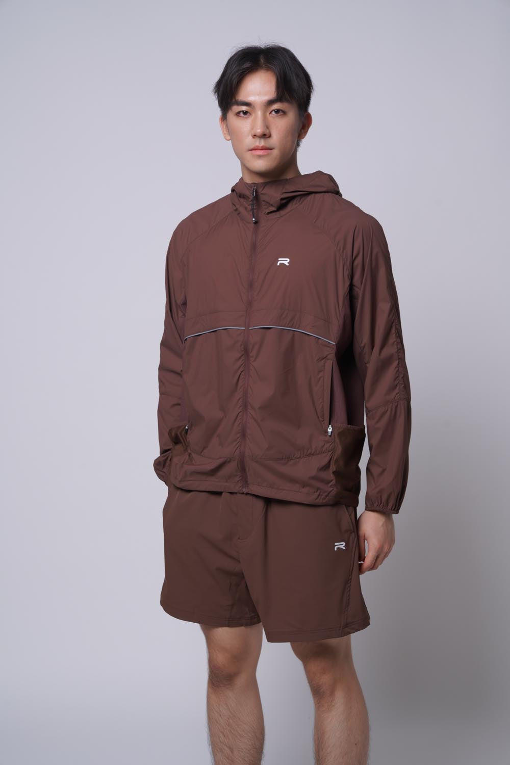 Asian male model standing wearing the Ramsports MatchDay Core Short in brown and a Ramsports brown jacket