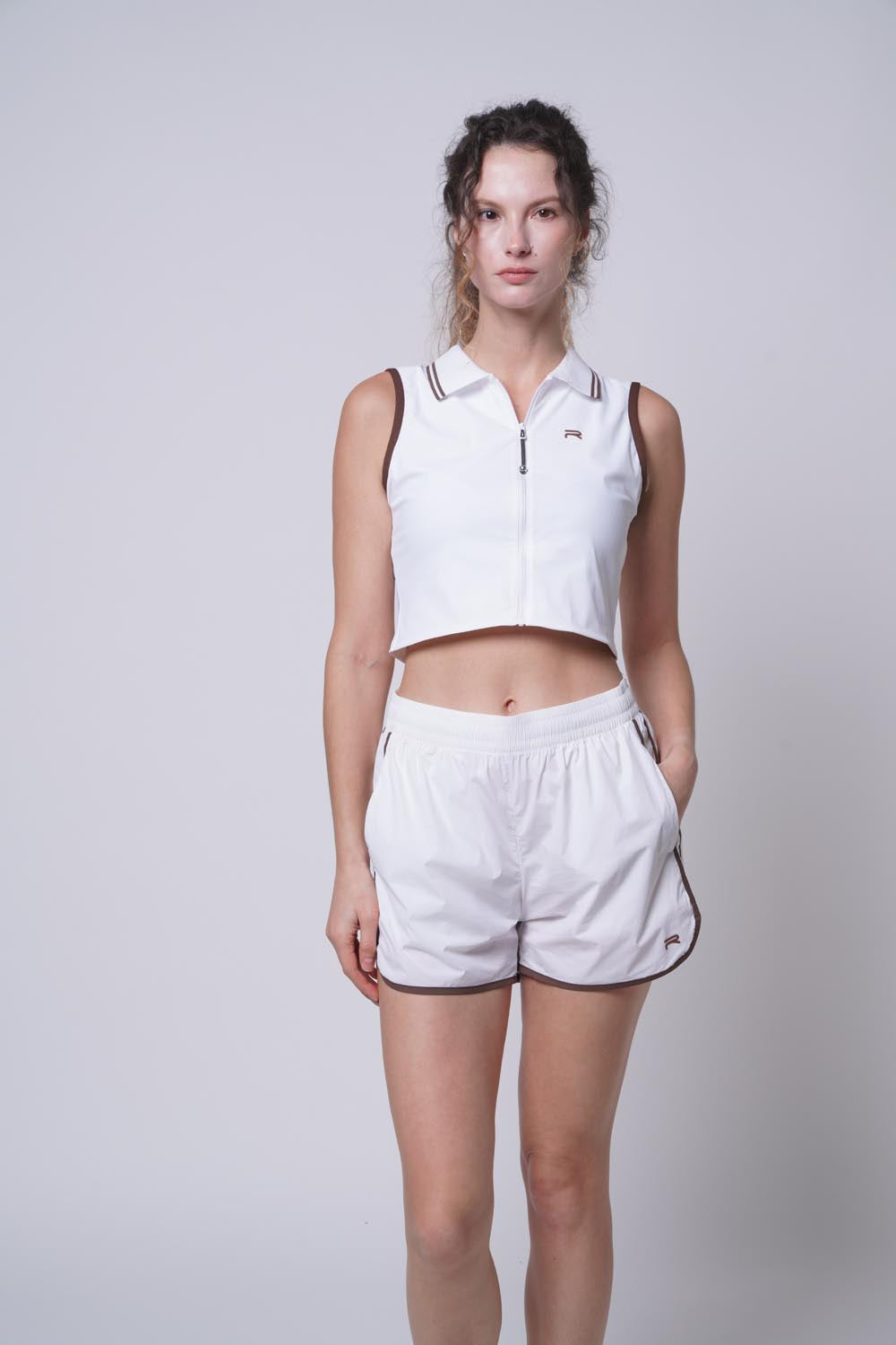 Female model with her hand on pocket wearing Ramsports serve zip crop polo in white