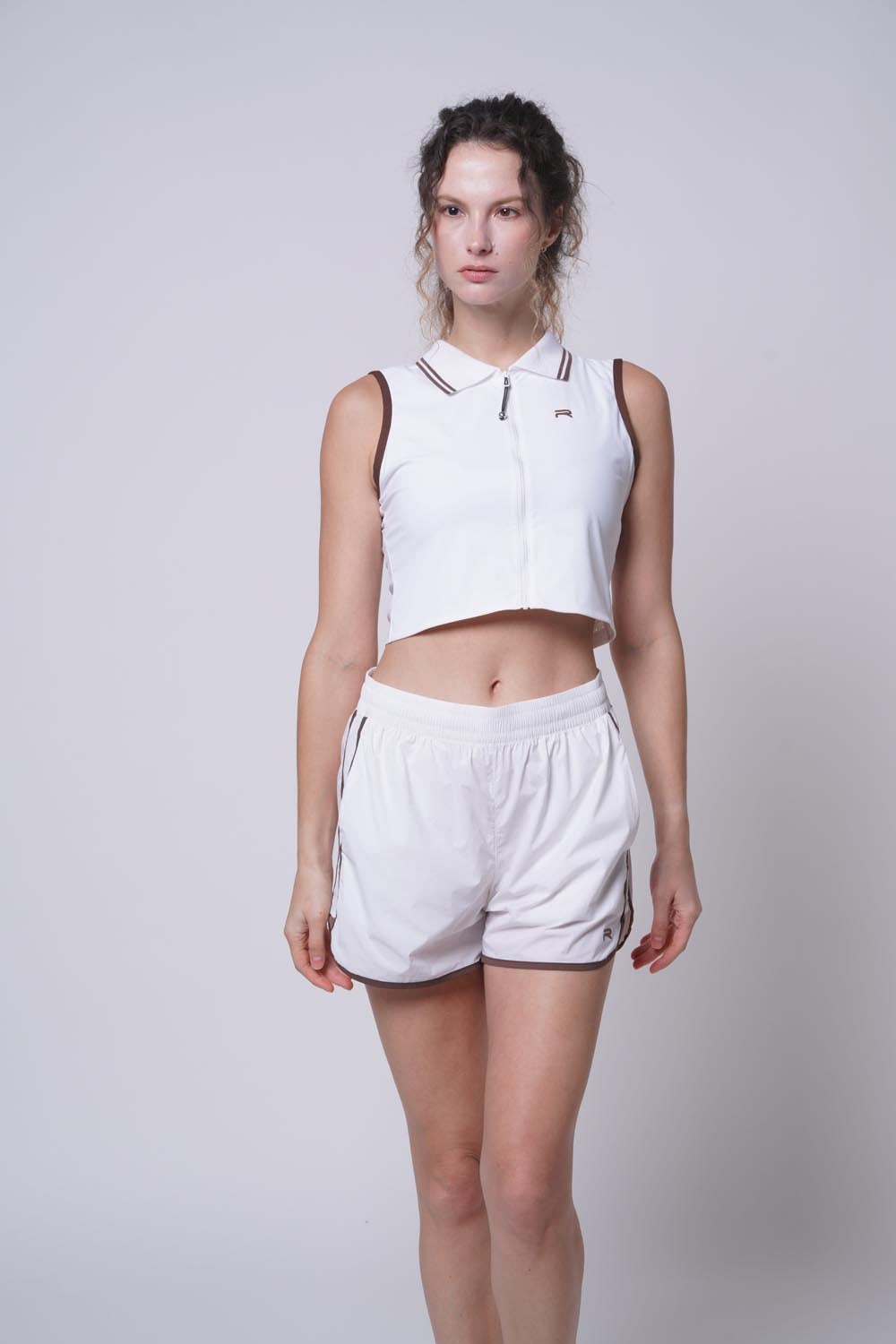 female model wearing the ramsports Flow Panel Split-Hem Short in white with sleeveless polo shirt.