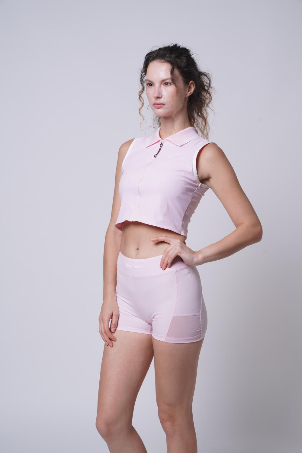 Female model with her hand on her left hip wearing Ramsports serve zip crop polo in pink