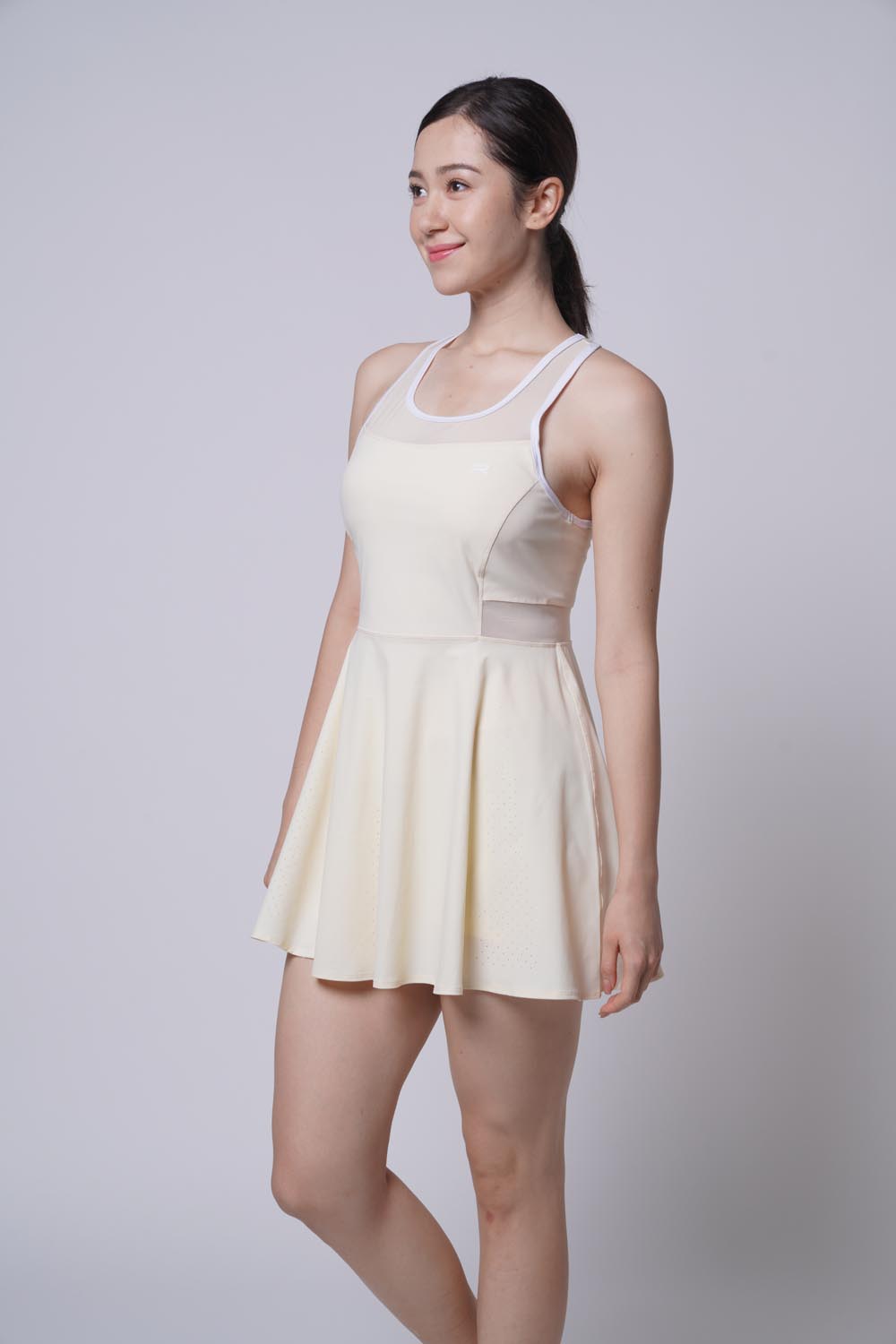 Asian female model smiling and looking away as she's wearing the Ramsports Racer Flare Dress in beige