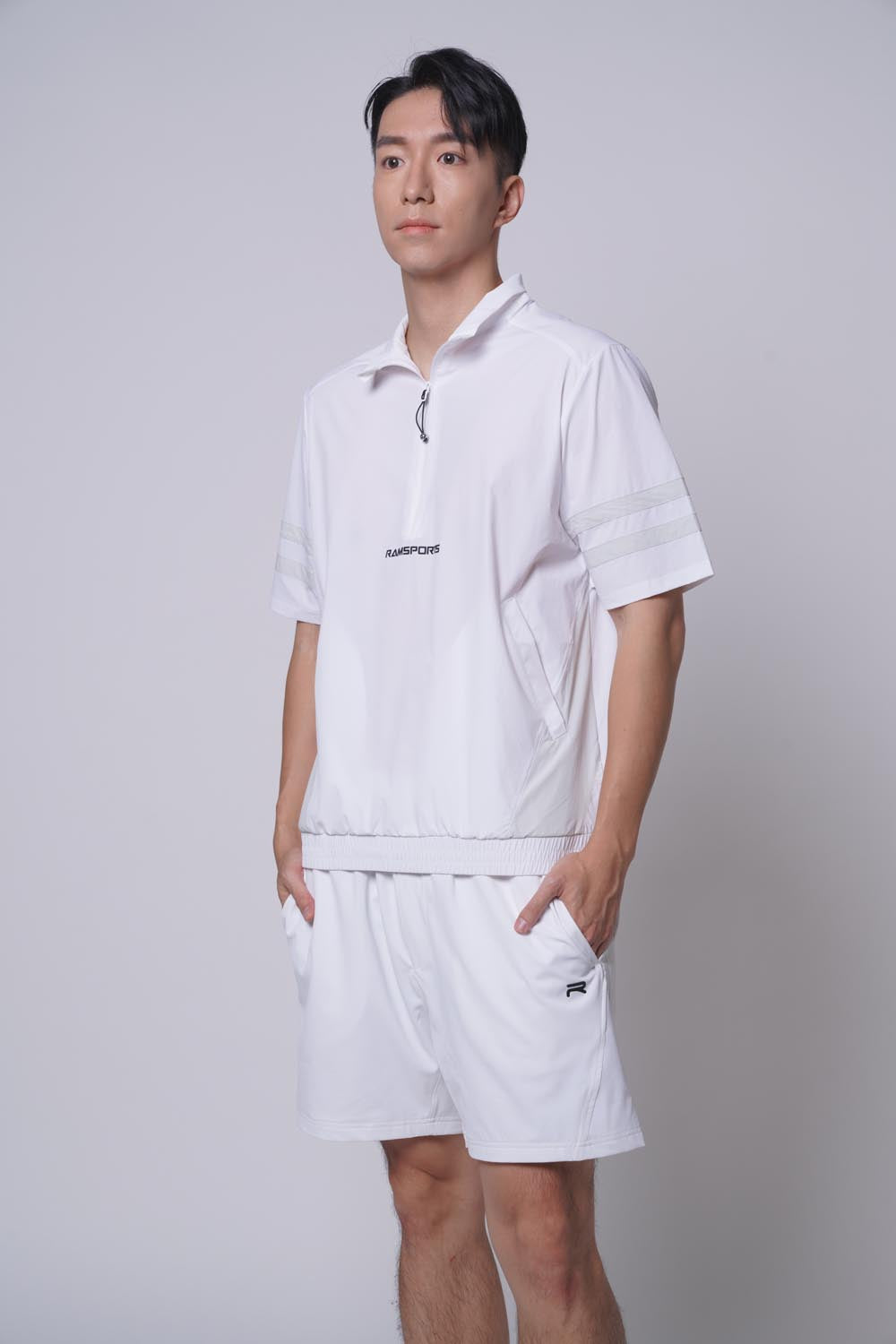 Another asian male model standing sideways, looking away at the camera with both hands on pocket, wearing of Ramsports MatchDay Core Short in white