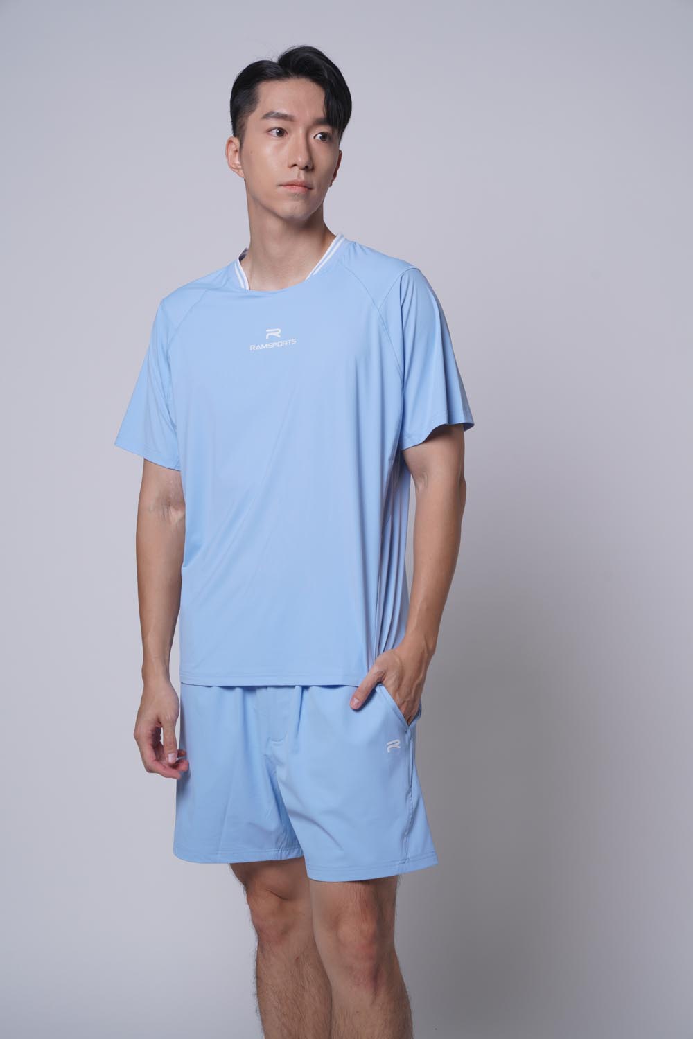 Asian male model with hands on pocket, wearing Ramsports Edge Line Raglan Tee in blue