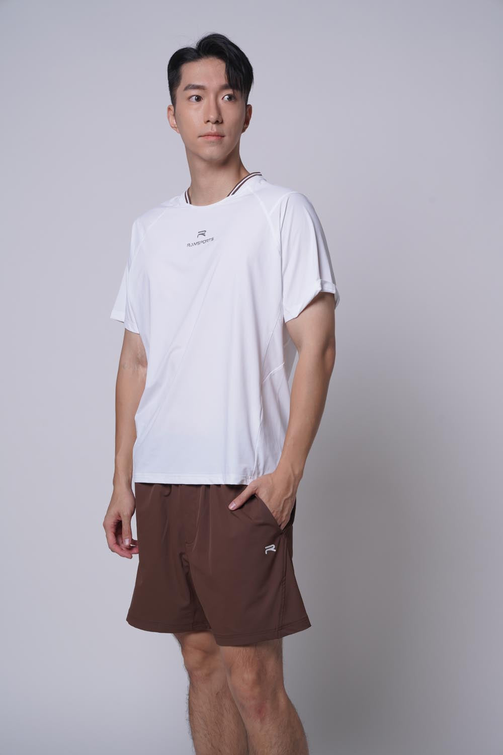 Male model standing sideways, one hands on pocket, wearing ramsports Edge Line Raglan Tee in white with brown shorts