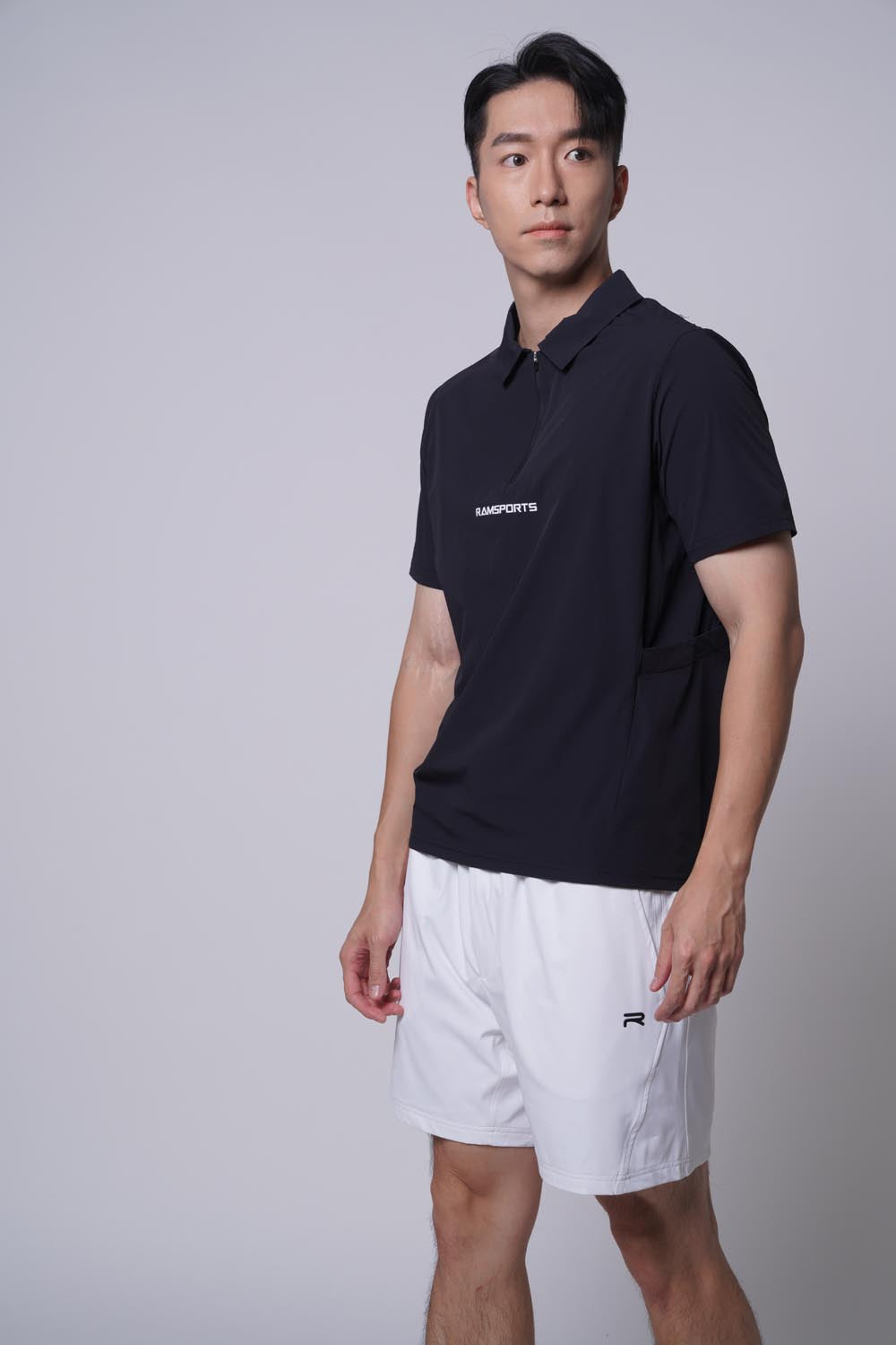 Asian male model standing sideways, looking away at the camera wearing of Ramsports MatchDay Core Short in white and a black top