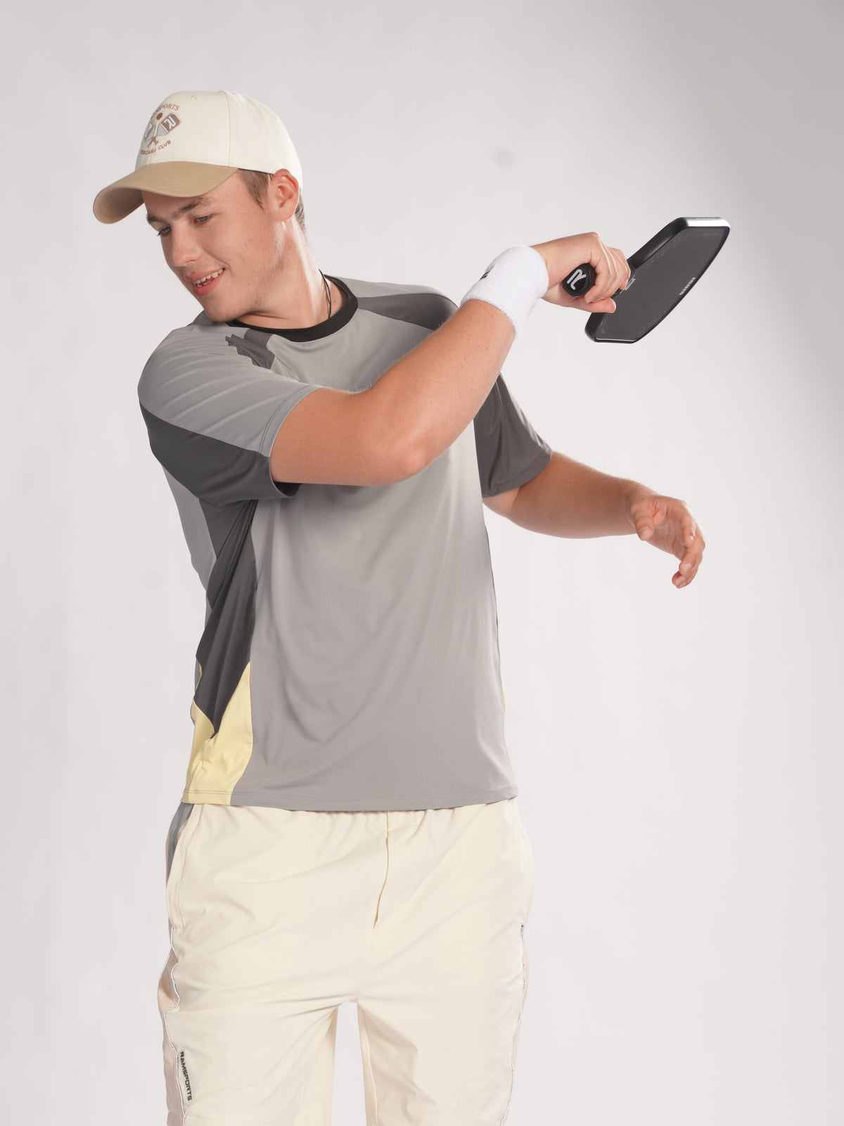 Man in gray shirt, beige pants with beige cap holding a paddle on a white background