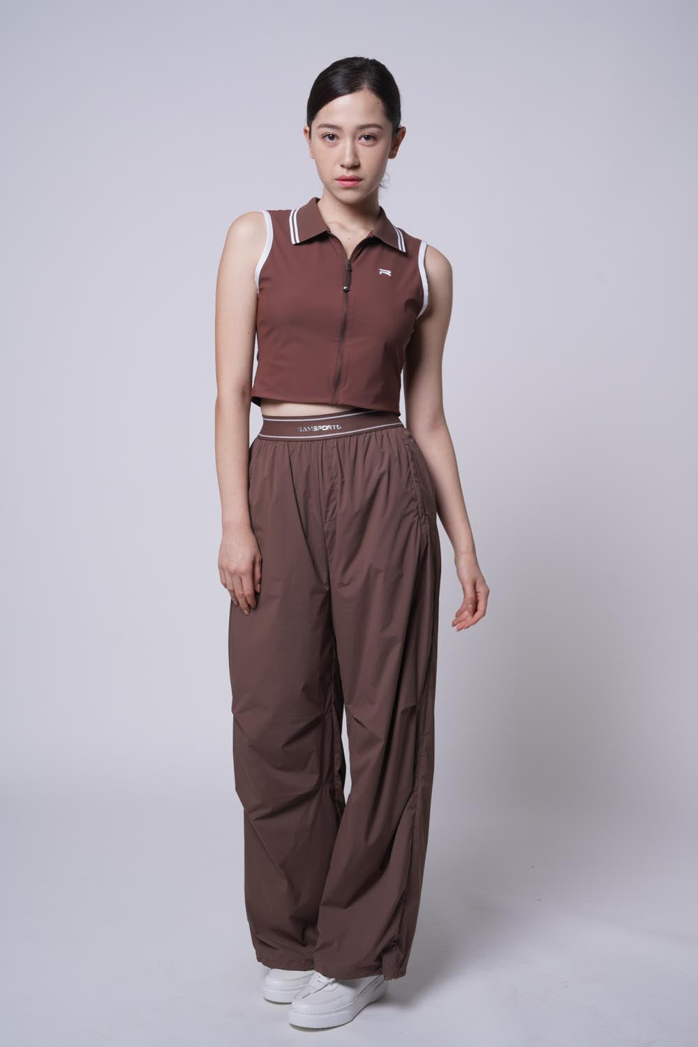 Full body picture of Asian female model wearing Ramsports serve zip crop polo in brown