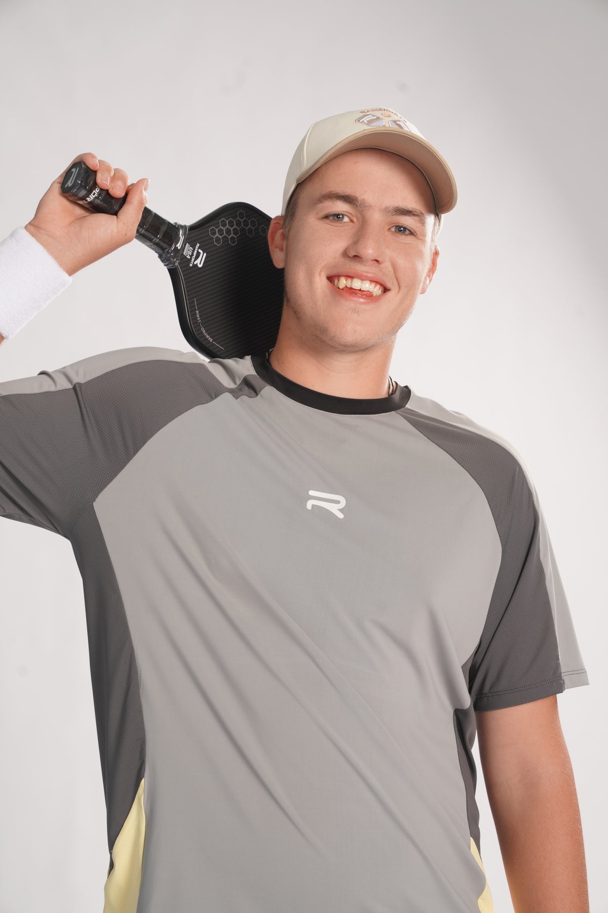man smiling wearing a gray ramsport shirt in a plain background with a paddle over his neck.